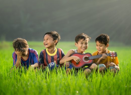 four boys laughing and sitting on grass during daytime